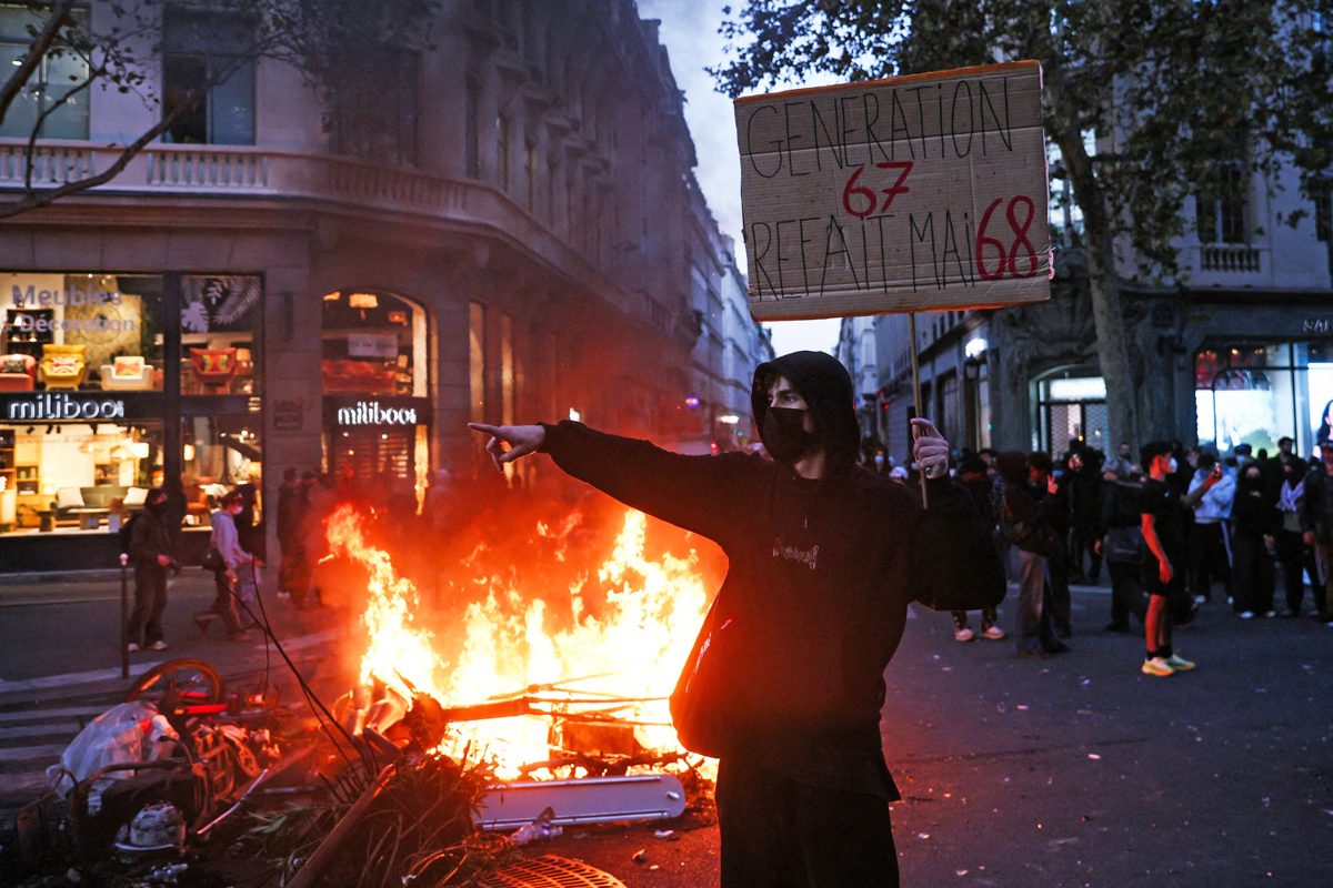 Protester pointing beside a burning barricade in Paris